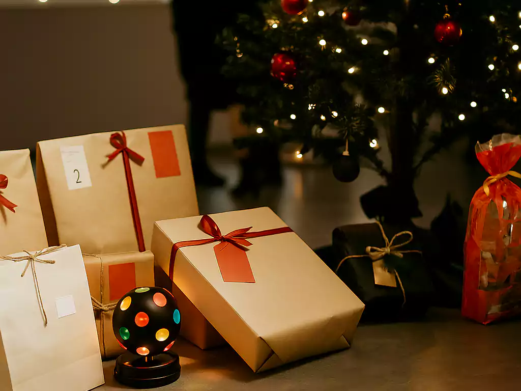 Assorted Christmas gifts wrapped in kraft paper and red ribbons under a decorated tree with festive lights